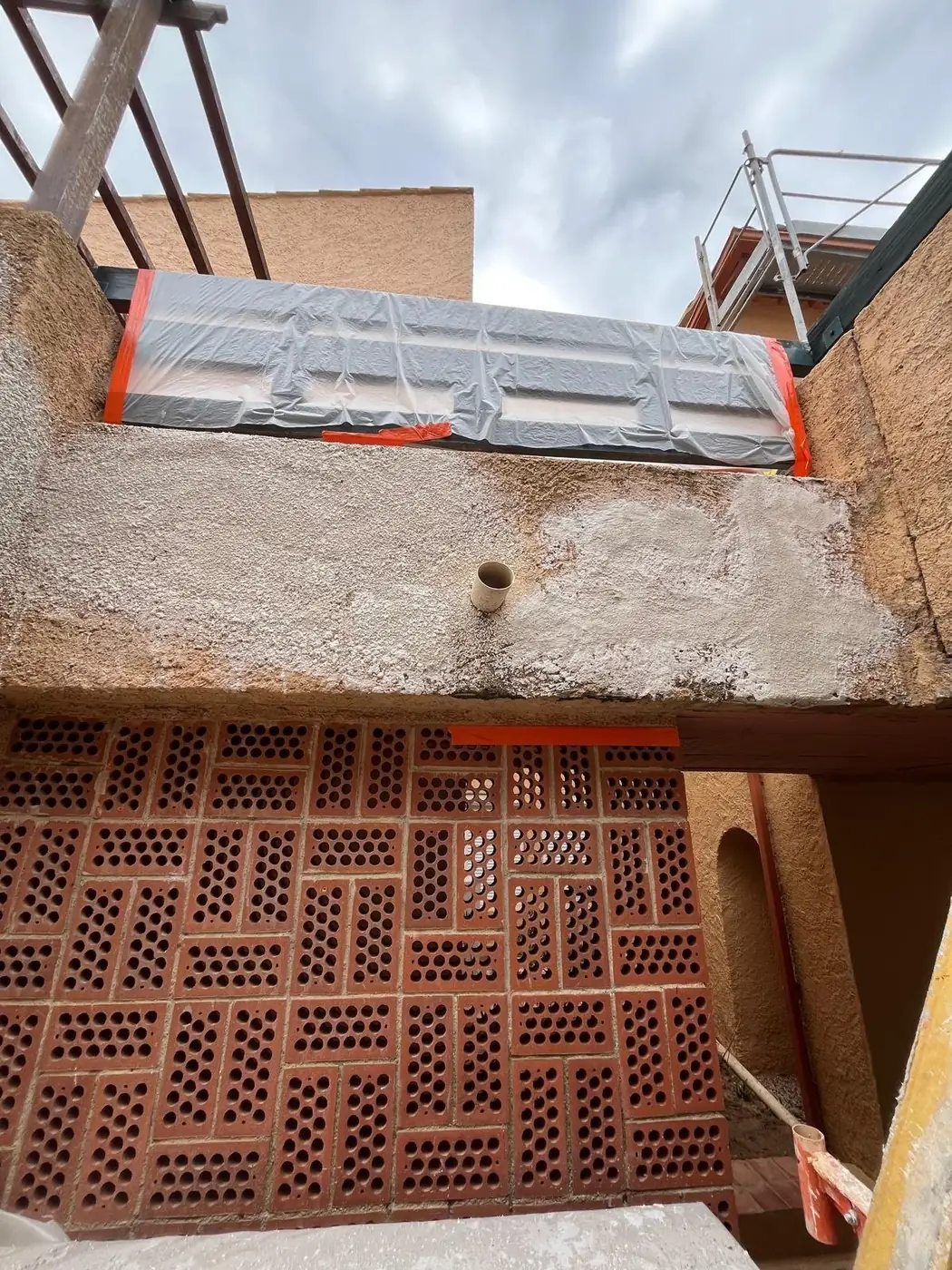Mur de briques alvéolées sous un balcon, enduit en cours de reprise sur un chantier des Pyrénées-Orientales (66)